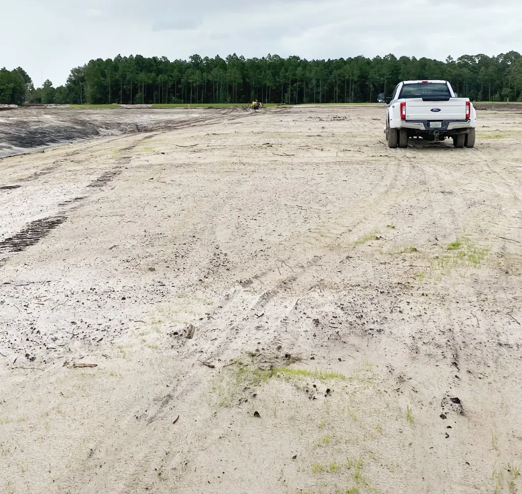 Bare sandy job site with only sparse sprouts on seed day