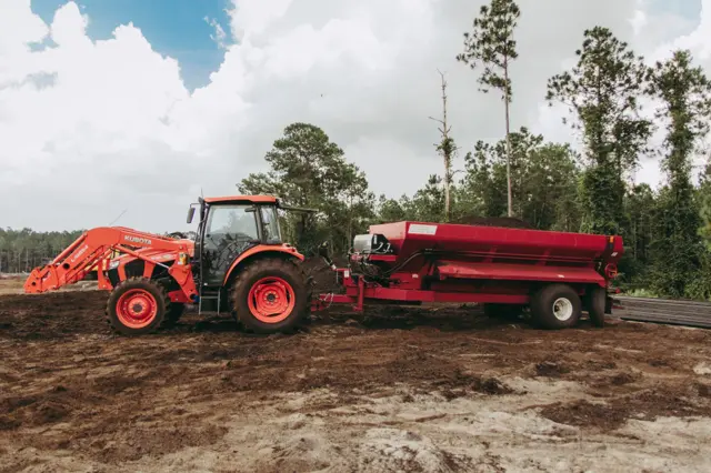 Tractor pulling a red spreader loaded with Class AA compost