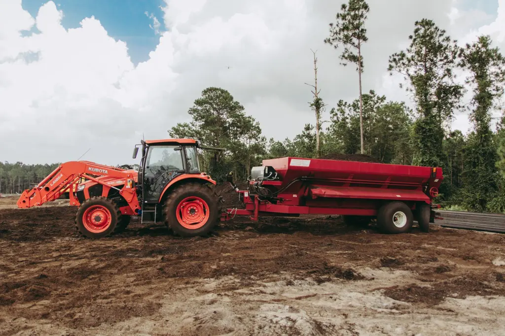 Tractor pulling a red spreader loaded with Class AA compost